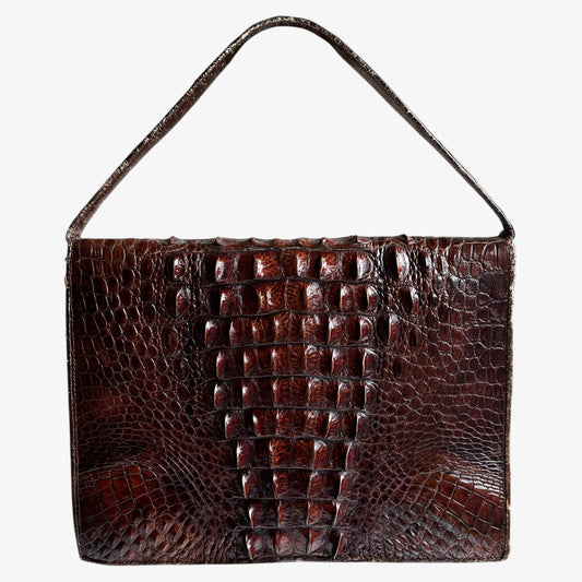 Back of a vintage 1950s brown crocodile leather shoulder bag on a white background.