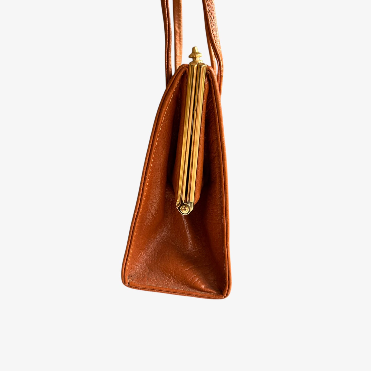 Side view of a vintage 1950s Freedex small orange leather frame bag on a white background.