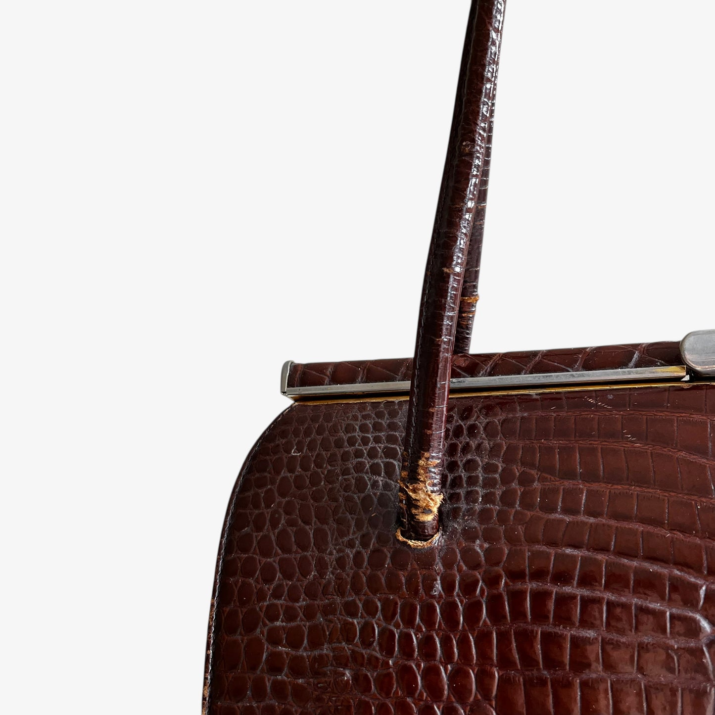 Close up of patina on the handle of a vintage 50s crocodile embossed brown leather shoulder bag.