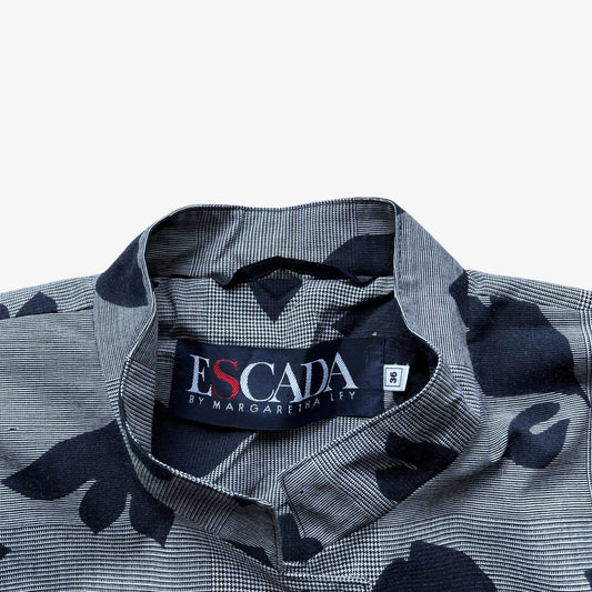 Close-up of a collared button-up shirt with a grey and black micro-check pattern and large black abstract leaf-like motifs. The neck label reads ESCADA by MARGARETHA LEY.