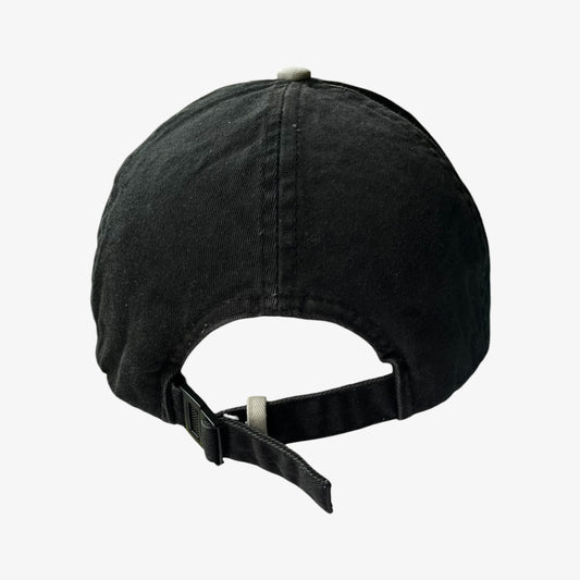 A black washed cotton baseball cap shown from the back, featuring a curved crown, a black adjustable strap with a plastic slider, and a small light grey button on top, set against a plain white background.