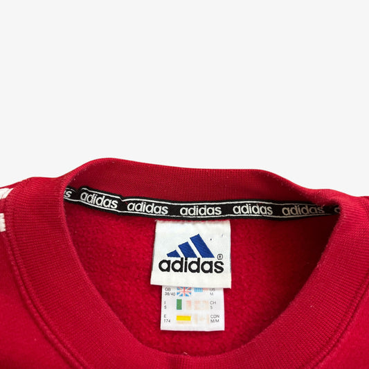 Close-up of Adidas logo and label on a red sweatshirt with black Adidas waistband.