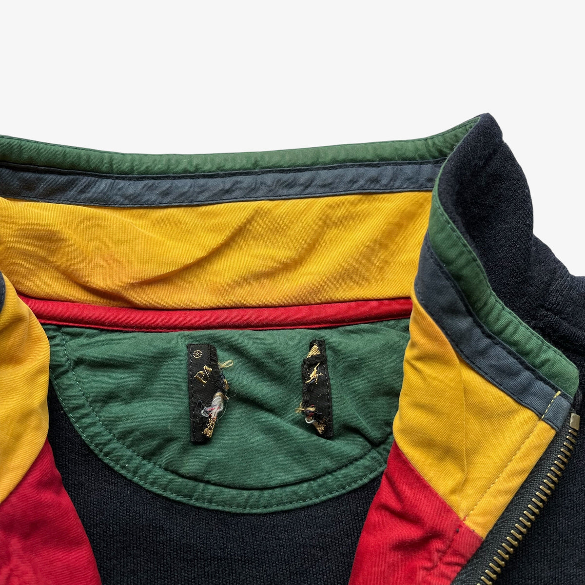Close-up of a colour-blocked fleece interior showing yellow, green, red, and dark navy panels, with two small embroidered patches on the green chest lining.