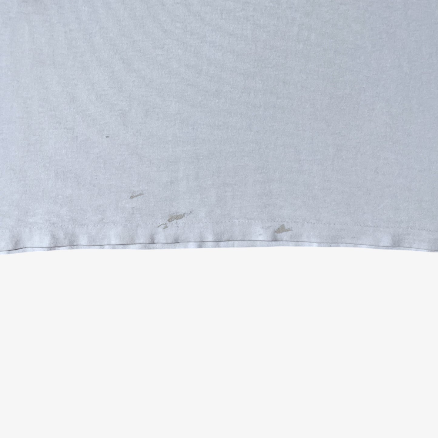 Hem of vintage 90s men's Stussy studio Jamaica reggae dance hall print white single stitch thrashed t-shirt.