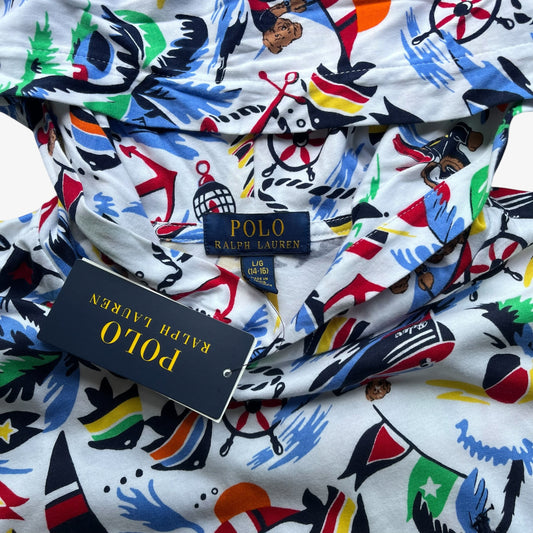 A close-up of a Polo Ralph Lauren hoodie featuring a colourful nautical-themed print on a white base. The print includes anchors, ships, compasses, and flags in blue, red, green, yellow, and black.