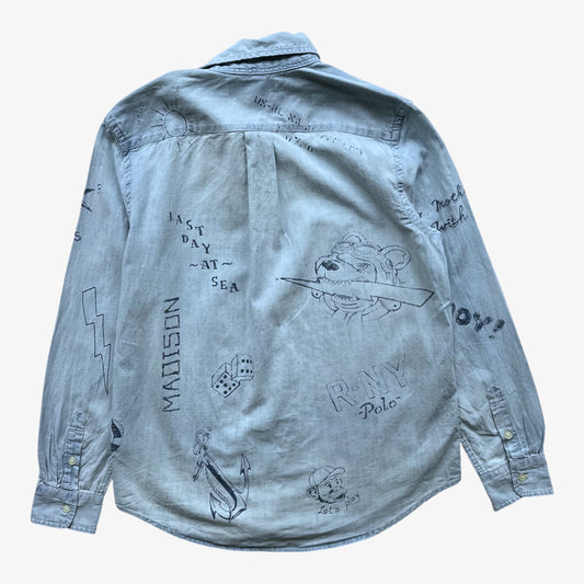 A light blue women's Ralph Lauren denim shirt jacket shown from the back, featuring various black line-art illustrations and text prints including 'Madison', 'Ray Polo', and '1st Day at Sea'.