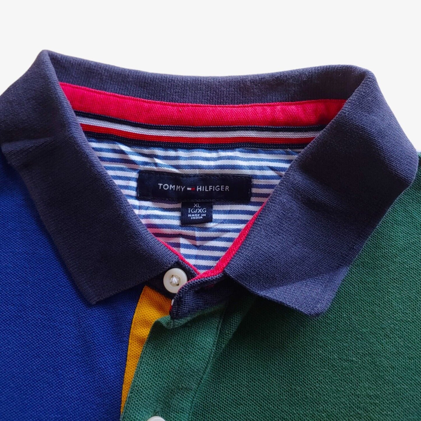 Label of colour blocked Tommy Hilfiger polo shirt with an embroidered chest logo, featuring a combination of blue, red, green, and grey colours.