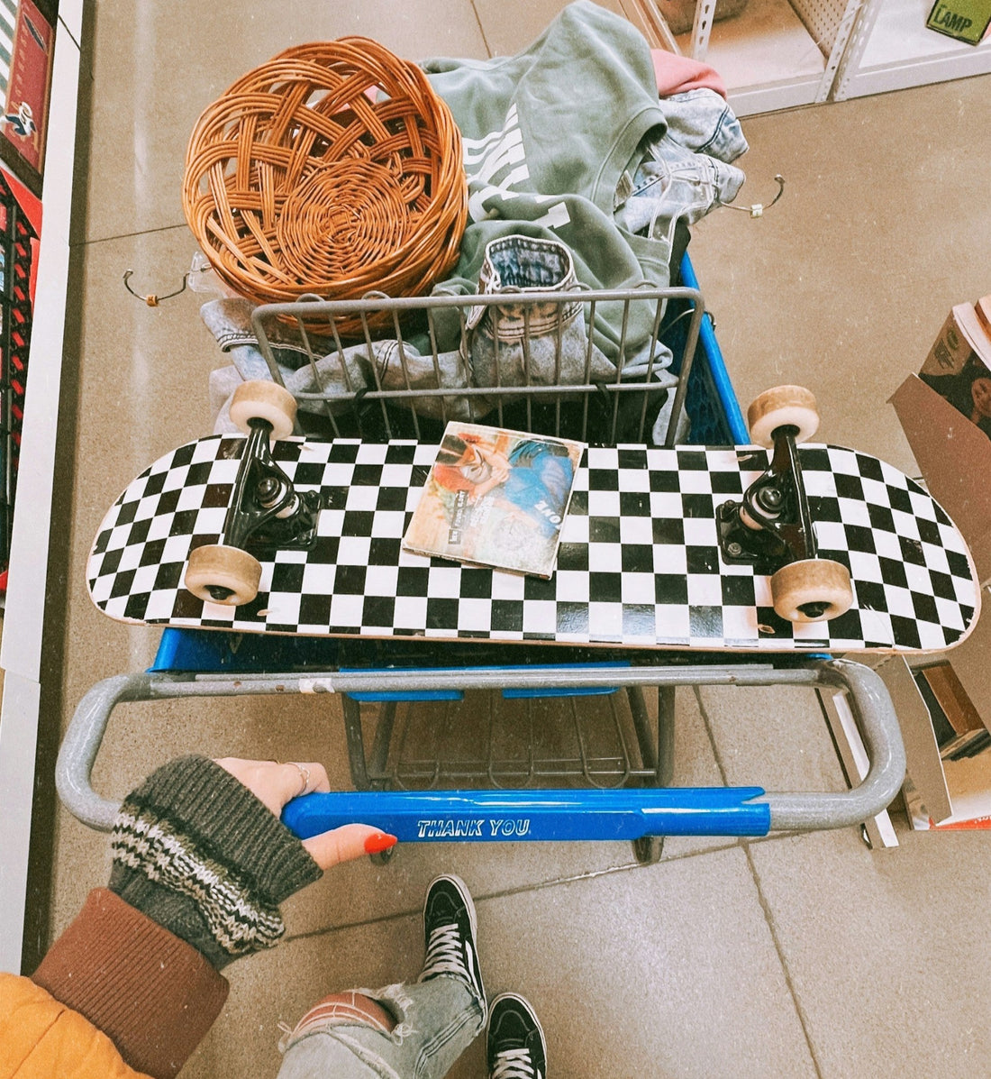 Close up of a shopping chart filled with vintage Y2K clothing and accessories, including a skateboard.