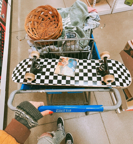 Close up of a shopping chart filled with vintage Y2K clothing and accessories, including a skateboard.