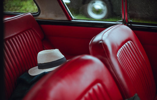 Close up of a folded vintage 80s men's suit and neatly placed trilby hat inside of a classic car's red leather seating.