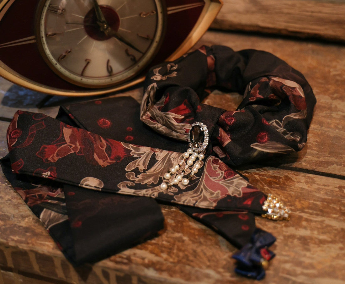 Vintage 80s abstract floral print black silk tie laid on a wooden table next to an art deco clock.