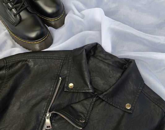 Close up of a men's vintage 90s black leather biker jacket and a pair of leather Dr Martens shoes.