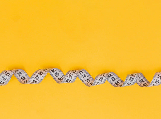 Close up of a measuring tape on a yellow background.