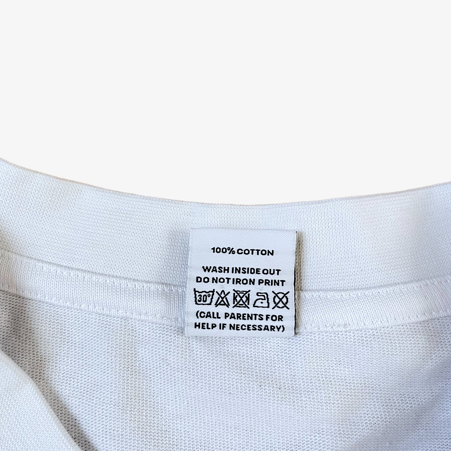 Care label of a white 100% organic cotton t-shirt with a graphic print featuring a Banksy styled cartoon character, police dogs and text that reads 'DREAMERS NEVER STOP creating'.