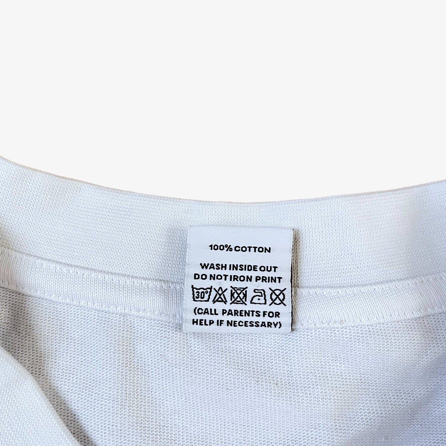 Care label of a white 100% organic cotton t-shirt with a graphic print featuring a Banksy styled cartoon character, police dogs and text that reads 'DREAMERS NEVER STOP creating'.