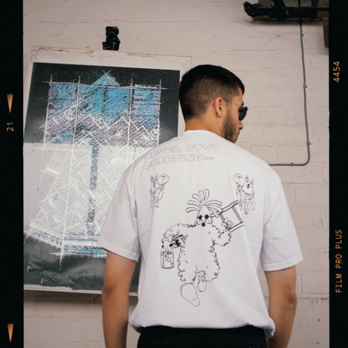 Modelled photo of the back of a white 100% organic cotton t-shirt with a graphic print featuring a Banksy styled cartoon character being chased by police dogs.