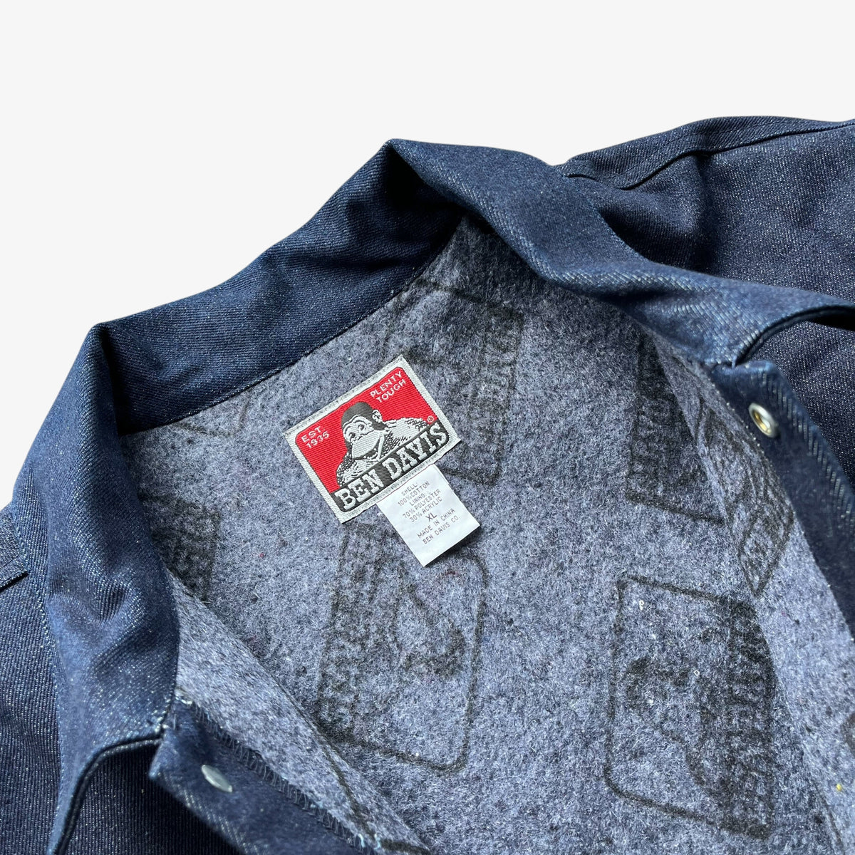 Close-up of a blue denim workwear jacket collar showing the interior blanket lining with a printed cardigan pattern and a visible red and white 'Ben Davis' brand label.