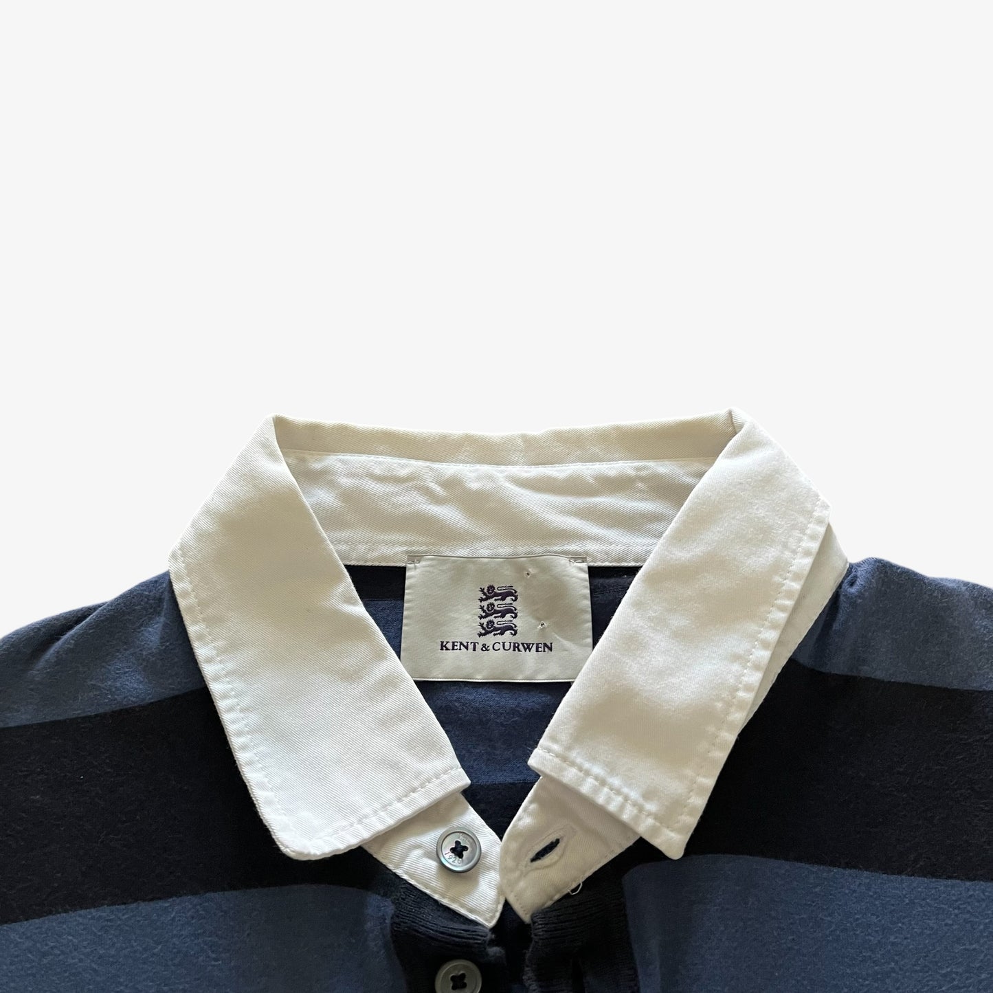 Close-up of a striped polo shirt collar with a cream-coloured collar and a visible Kent & Curwen label, set against a plain light background.