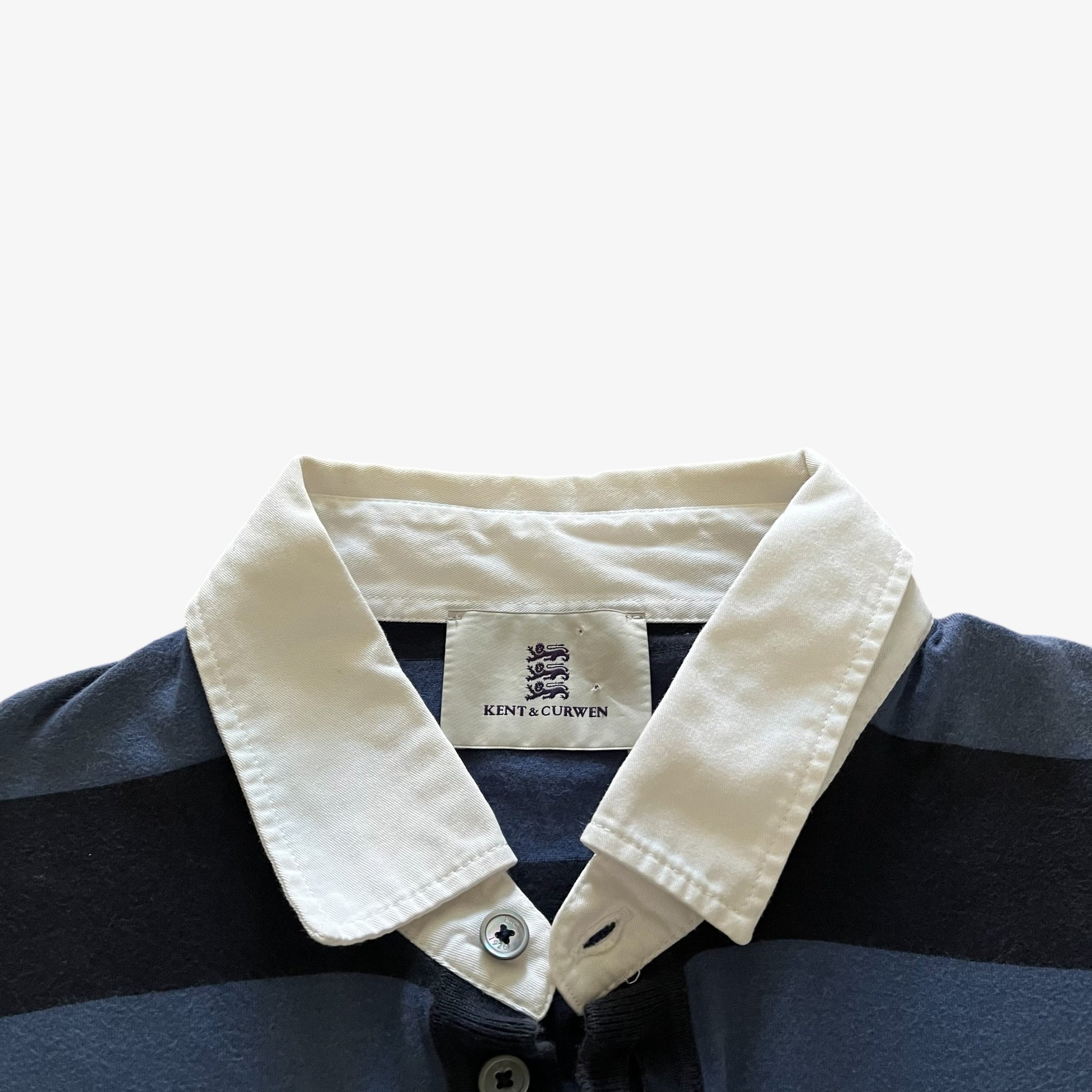 Close-up of a striped polo shirt collar with a cream-coloured collar and a visible Kent & Curwen label, set against a plain light background.