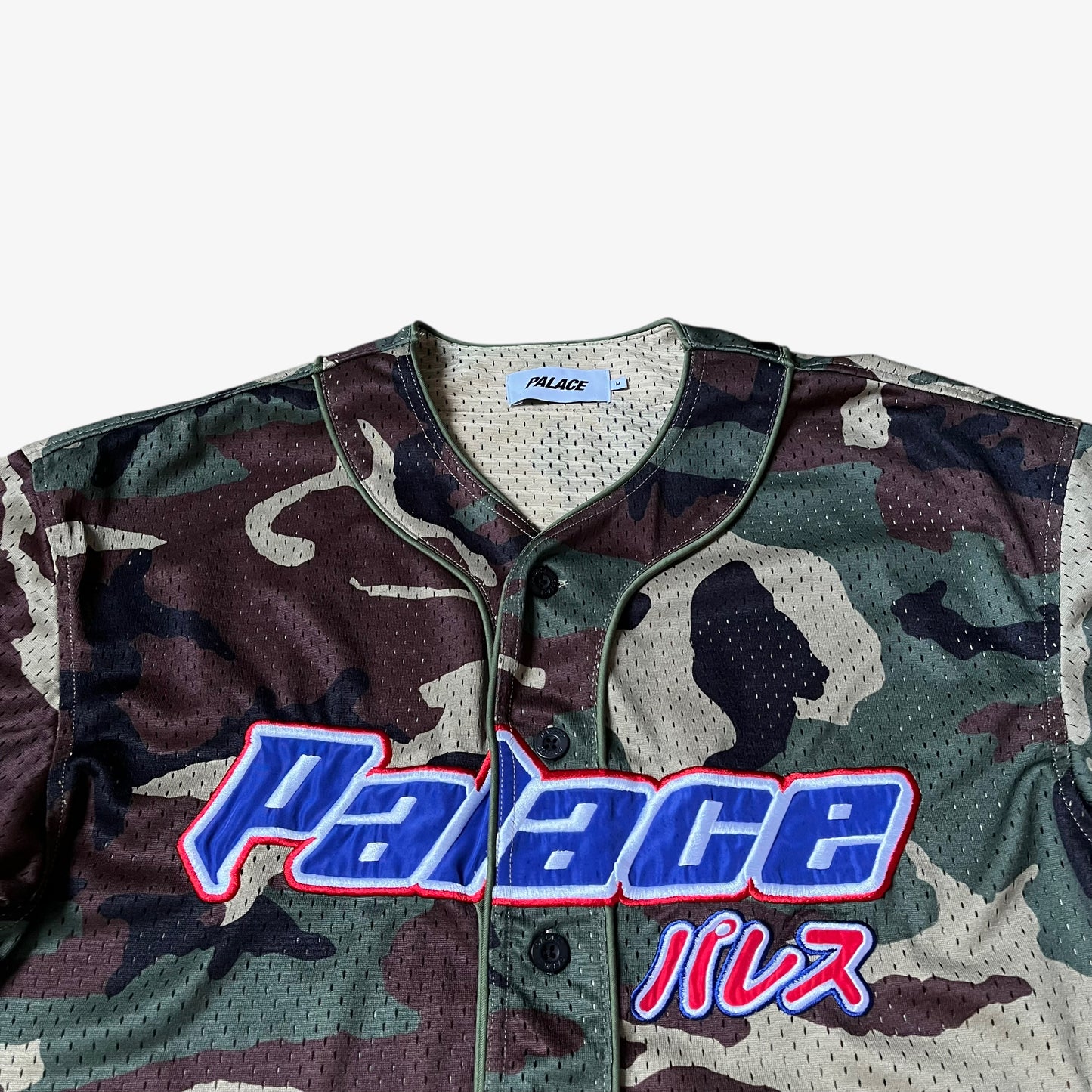Close up of embroidered spell out on men's Palace kawaii green camouflage baseball jersey.