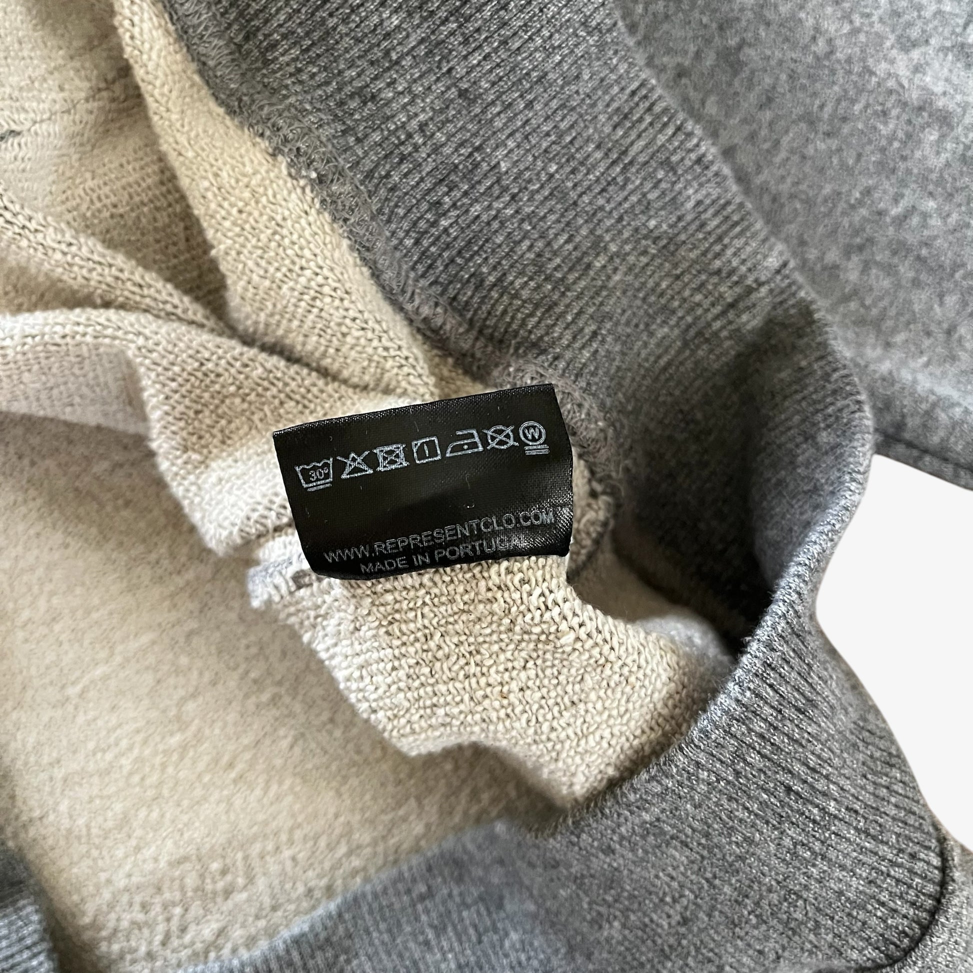 Close-up of a grey knit hoodie with a cream inner lining and a black care label reading made in Portugal.