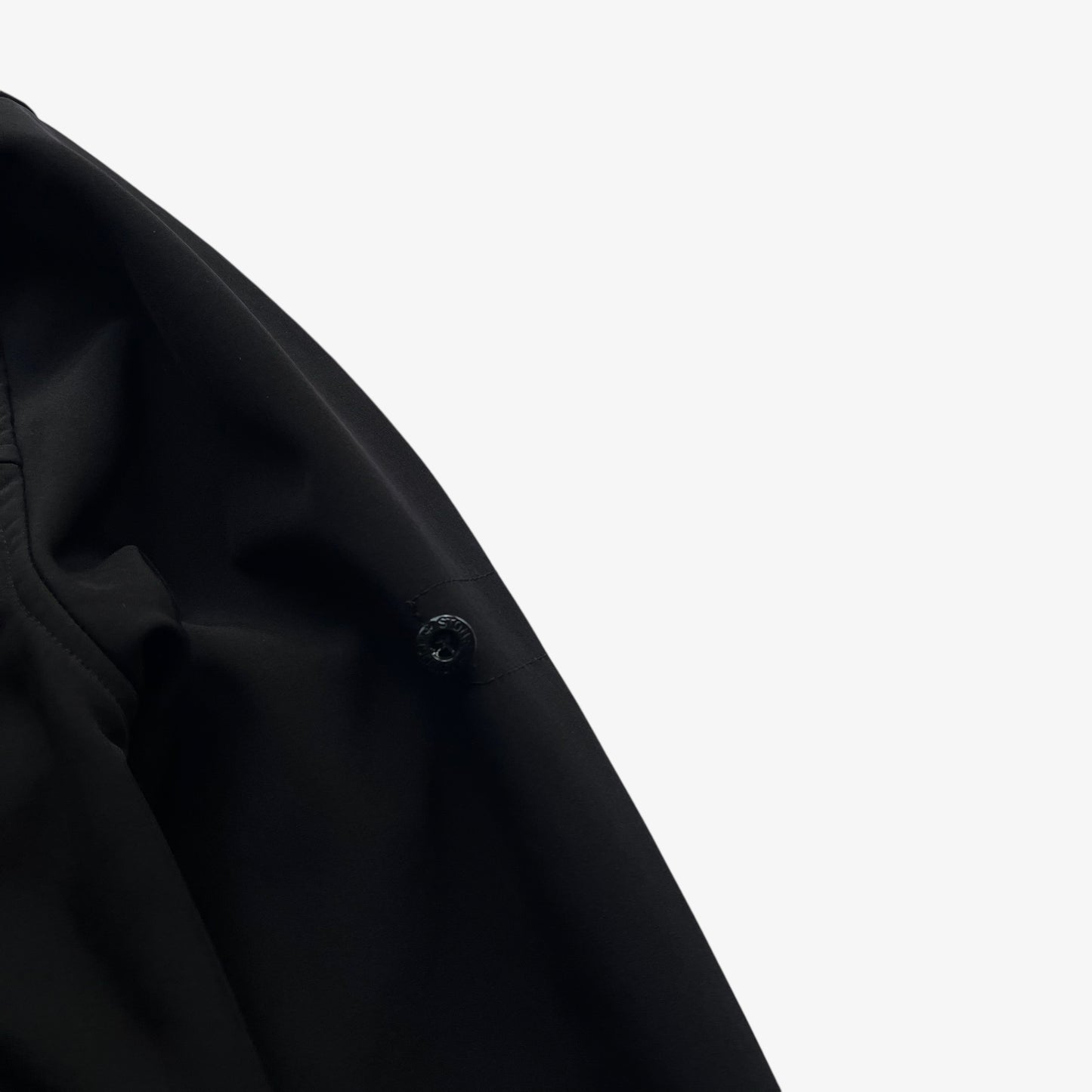 Badge of men's Stone Island Soft Shell R black utility jacket with foldable hood.