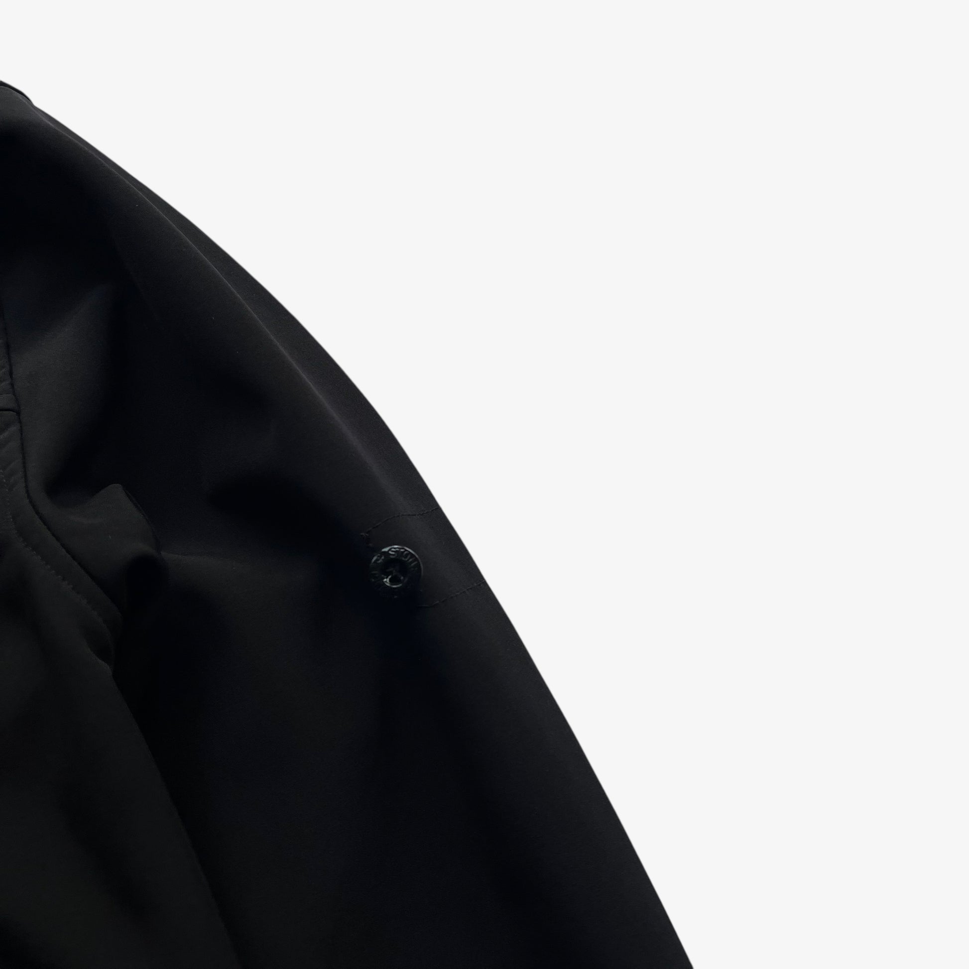 Badge of men's Stone Island Soft Shell R black utility jacket with foldable hood.