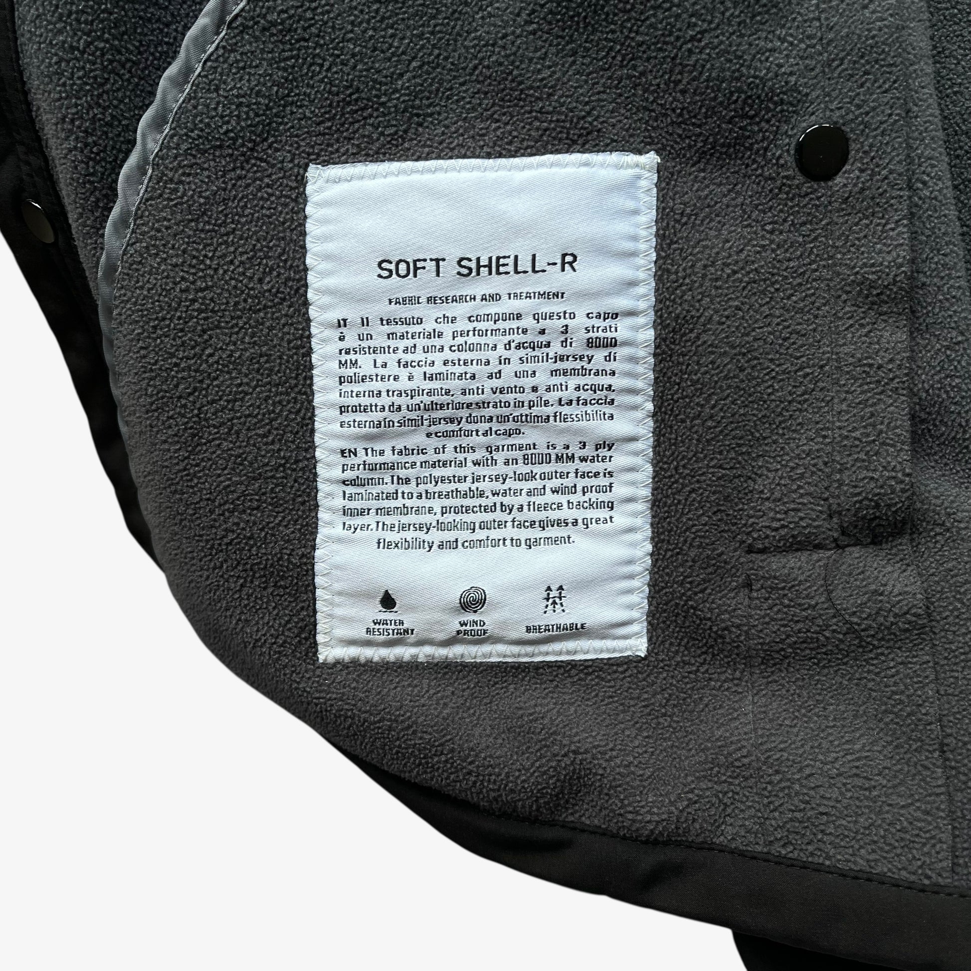 Soft Shell-R inside label of men's Stone Island black utility jacket with foldable hood.