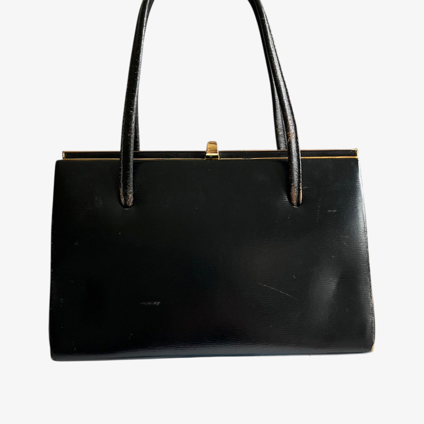 Back of a vintage 1950s black leather frame bag with a gold clasp on a white background.