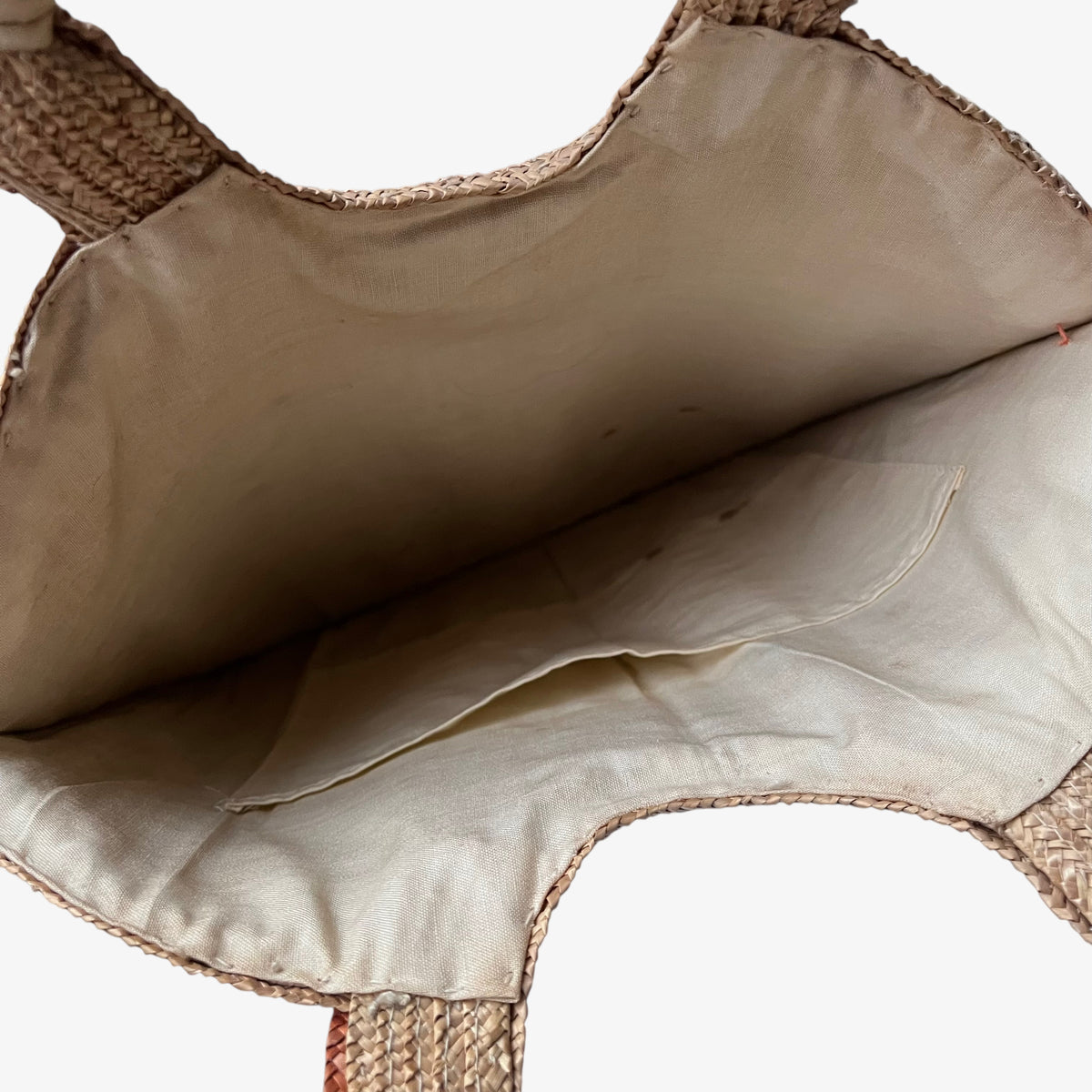 A close up of the pouch pocket inside a vintage 1950s crane and tree embroidered brown raffia tote bag.