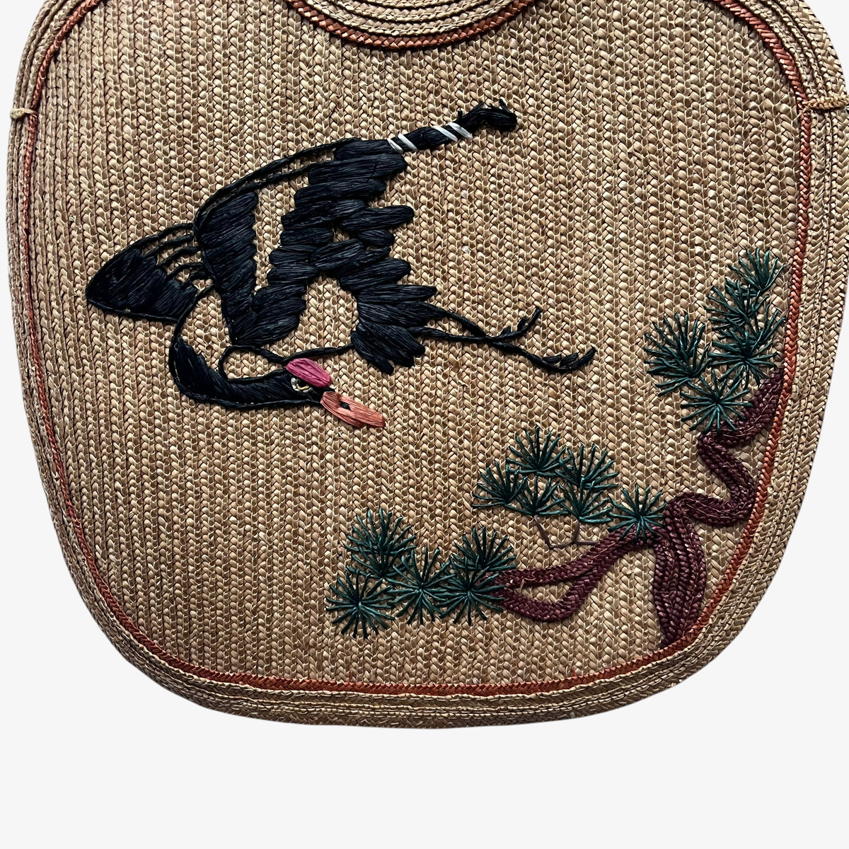 Close up of the crane and tree embroidery of a vintage 1950s brown raffia tote bag.