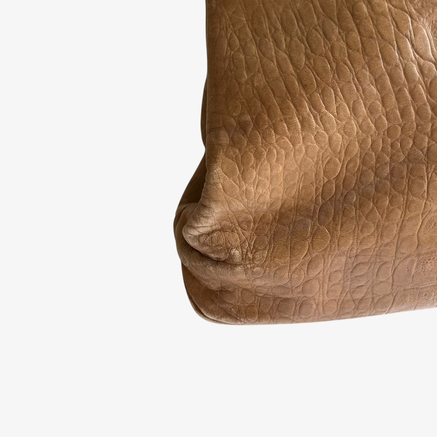Close up of wear on the corner of a vintage 1950s crocodile embossed light brown leather shoulder bag.