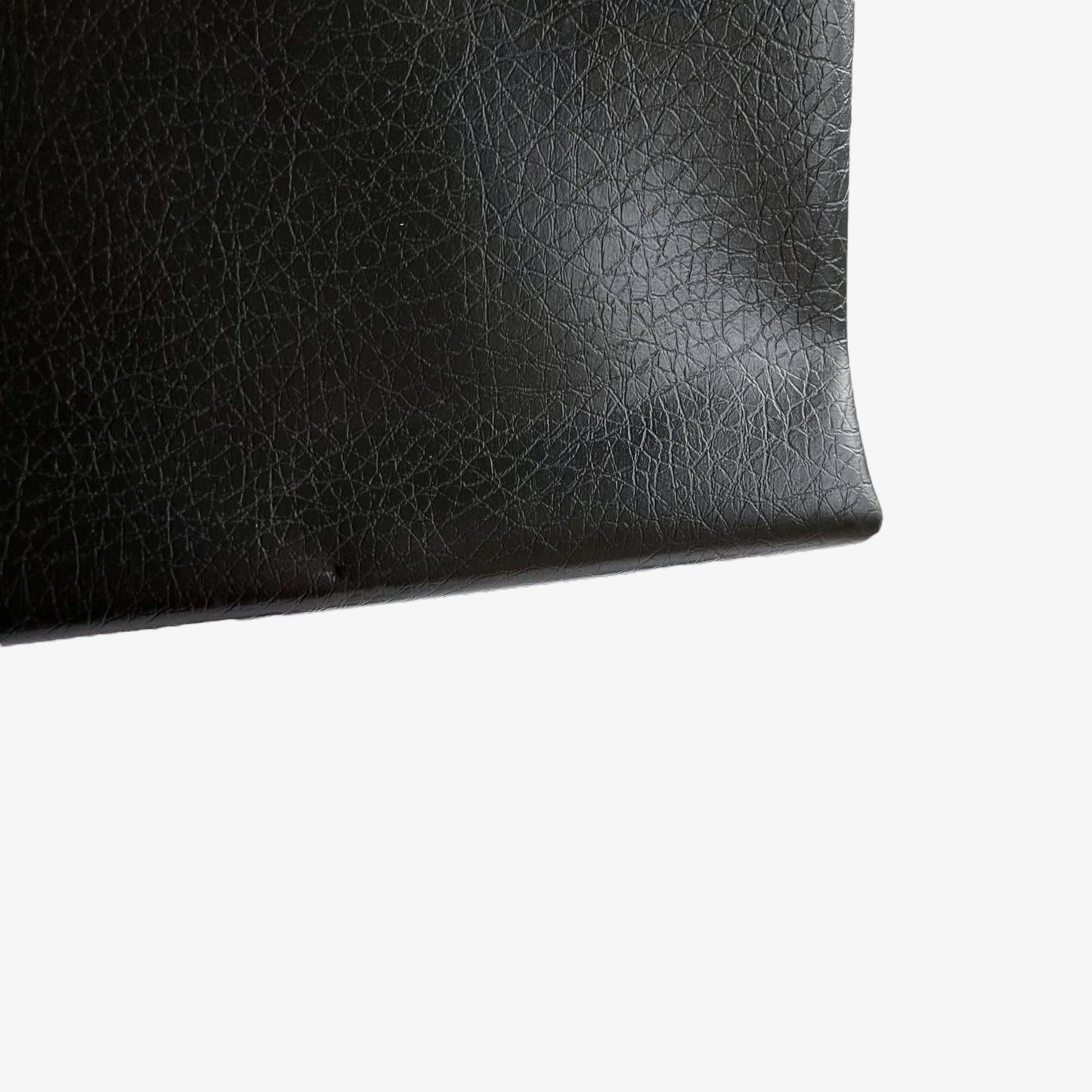 Close up of corner of a vintage 1960s black pebbled leather shoulder bag.