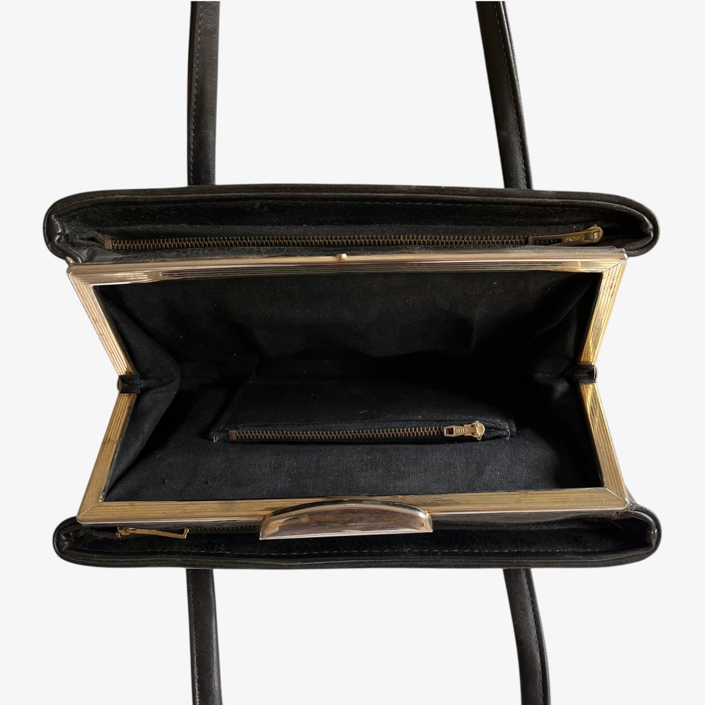 Close up of multiple zipped pockets inside of a vintage 1960s black pebbled leather shoulder bag.