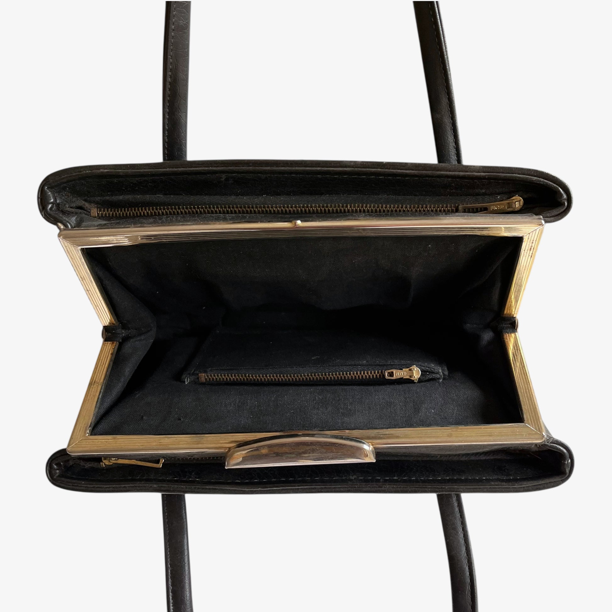 Close up of multiple zipped pockets inside of a vintage 1960s black pebbled leather shoulder bag.