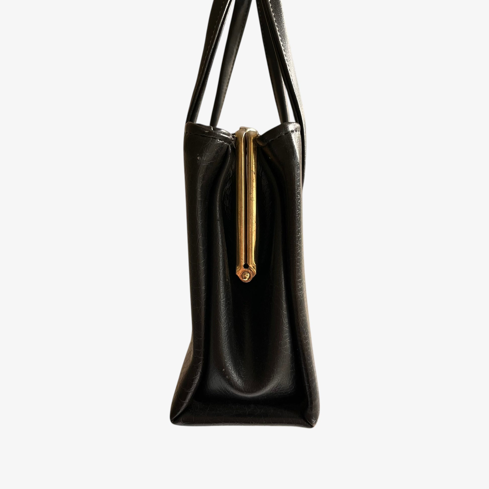 Side profile of a vintage 1960s black pebbled leather shoulder bag on a white background.