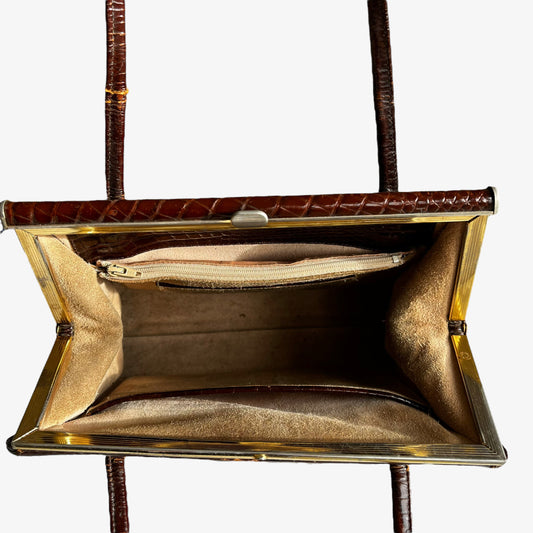 Close up of the suede lining and internal zipped pocket of a vintage 50s crocodile embossed brown leather shoulder bag.