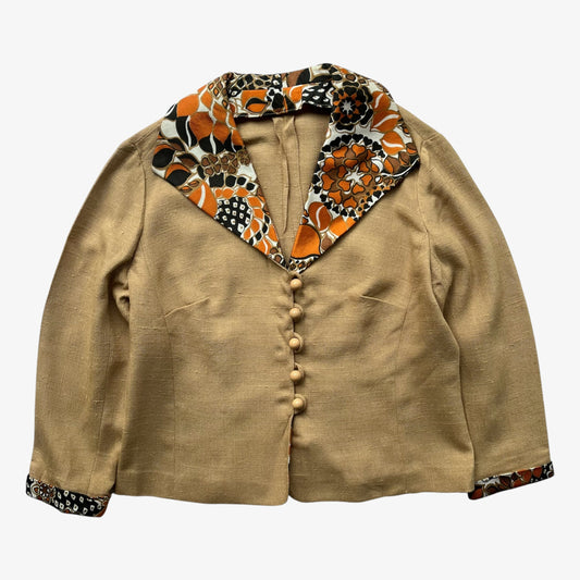 A 1970s women's Dereta tan linen jacket with an abstract floral patterned collar and cuffs in orange, black, and white, featuring a button front closure.