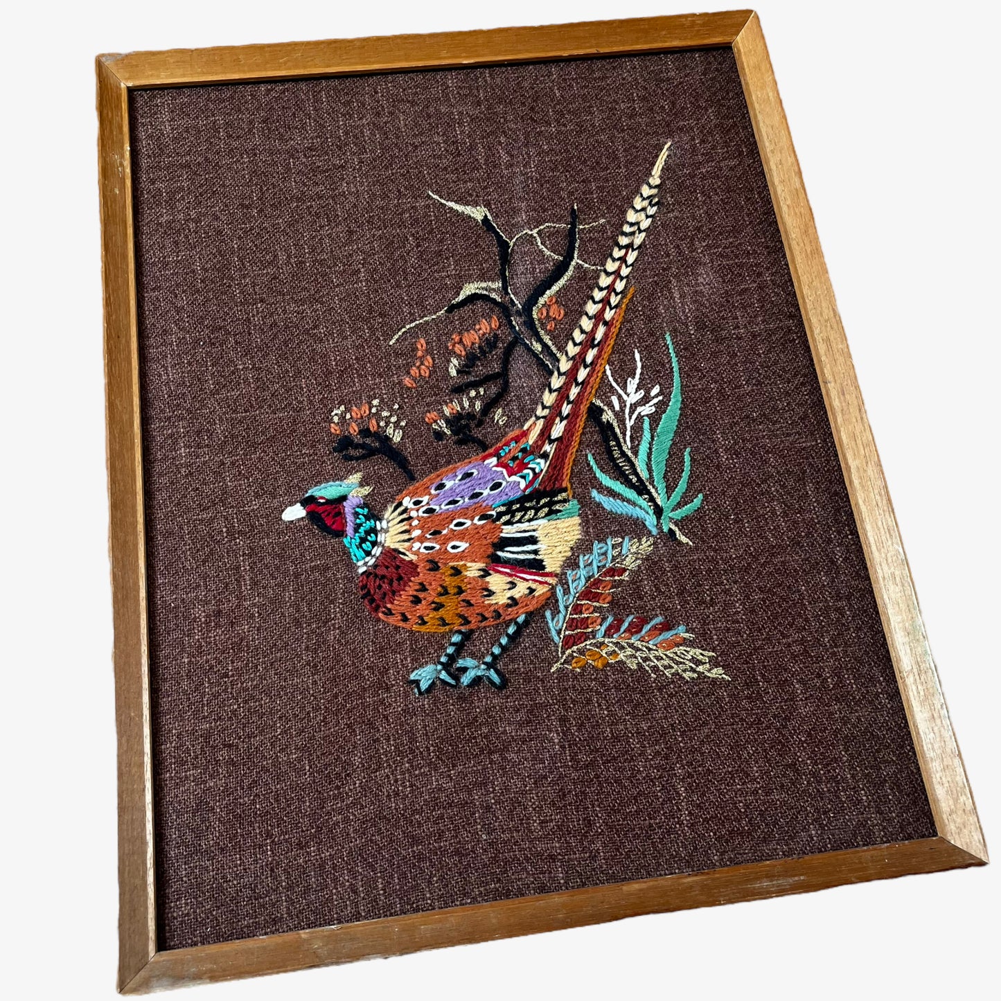 Close up of wooden framed vintage 70s peacock cross stitch tapestry.