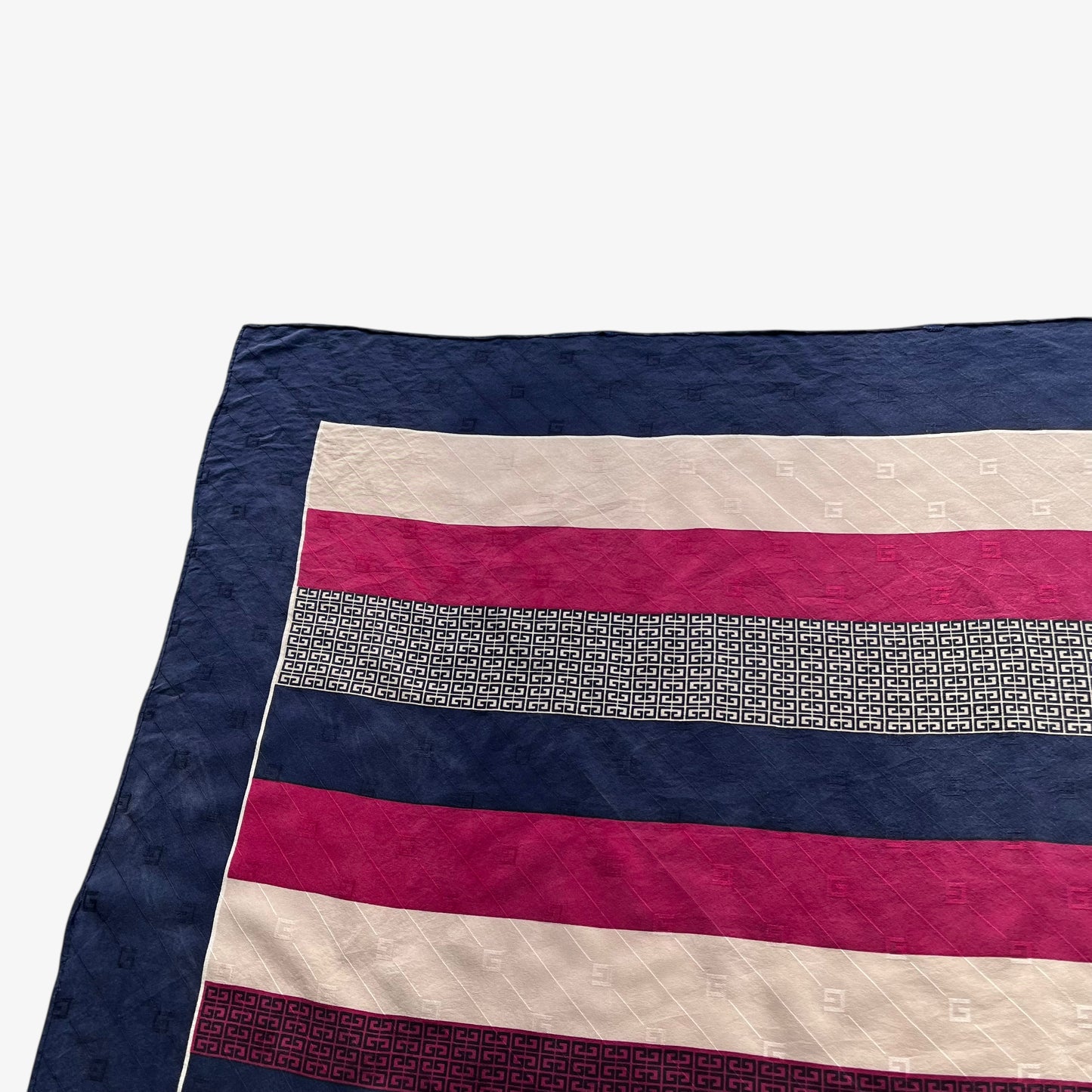 Close up of G motif of vintage 80s Givenchy red and navy striped silk scarf featuring a G monogram print.