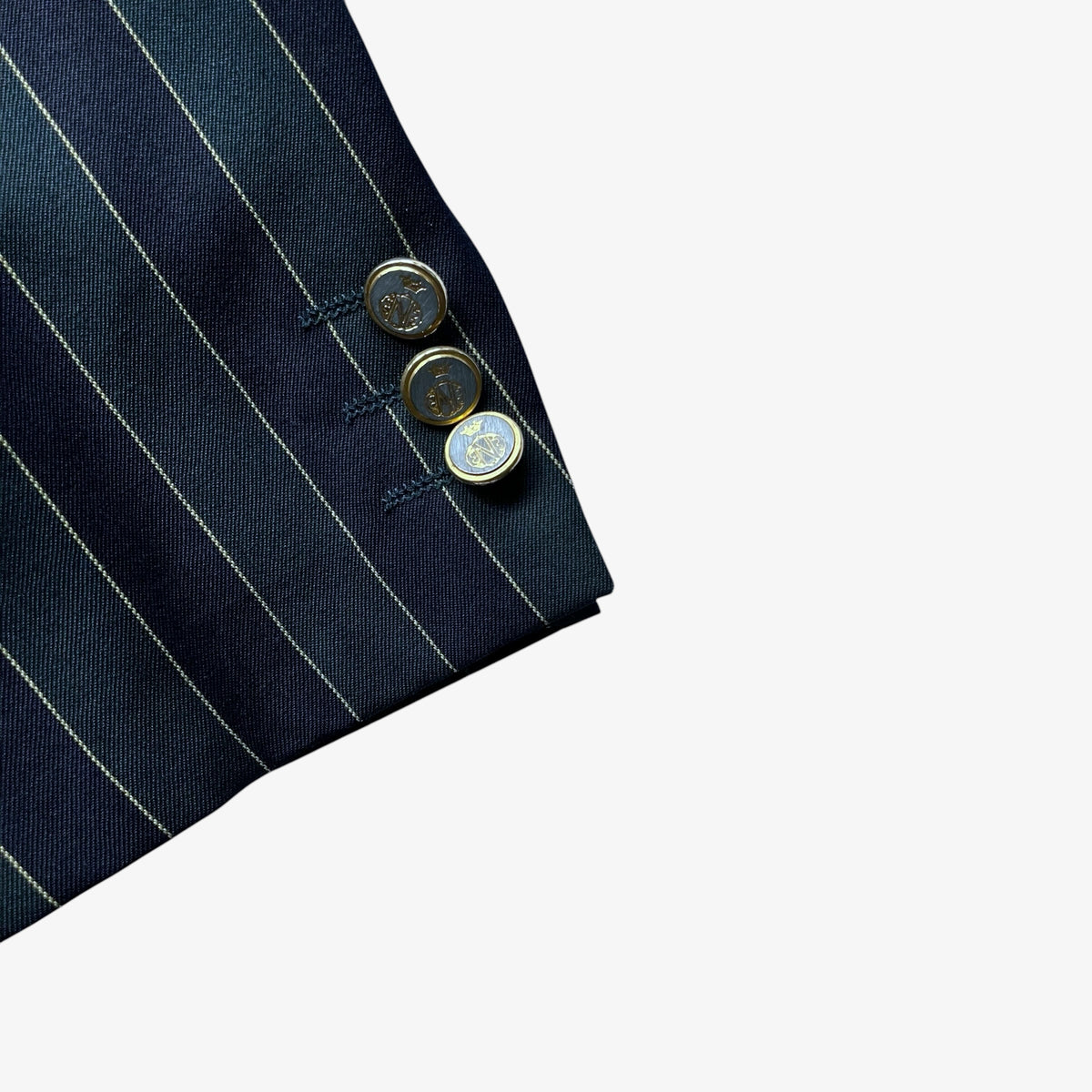 Close-up of a navy and green pinstripe blazer cuff with three decorative round buttons, shown on a plain white background.