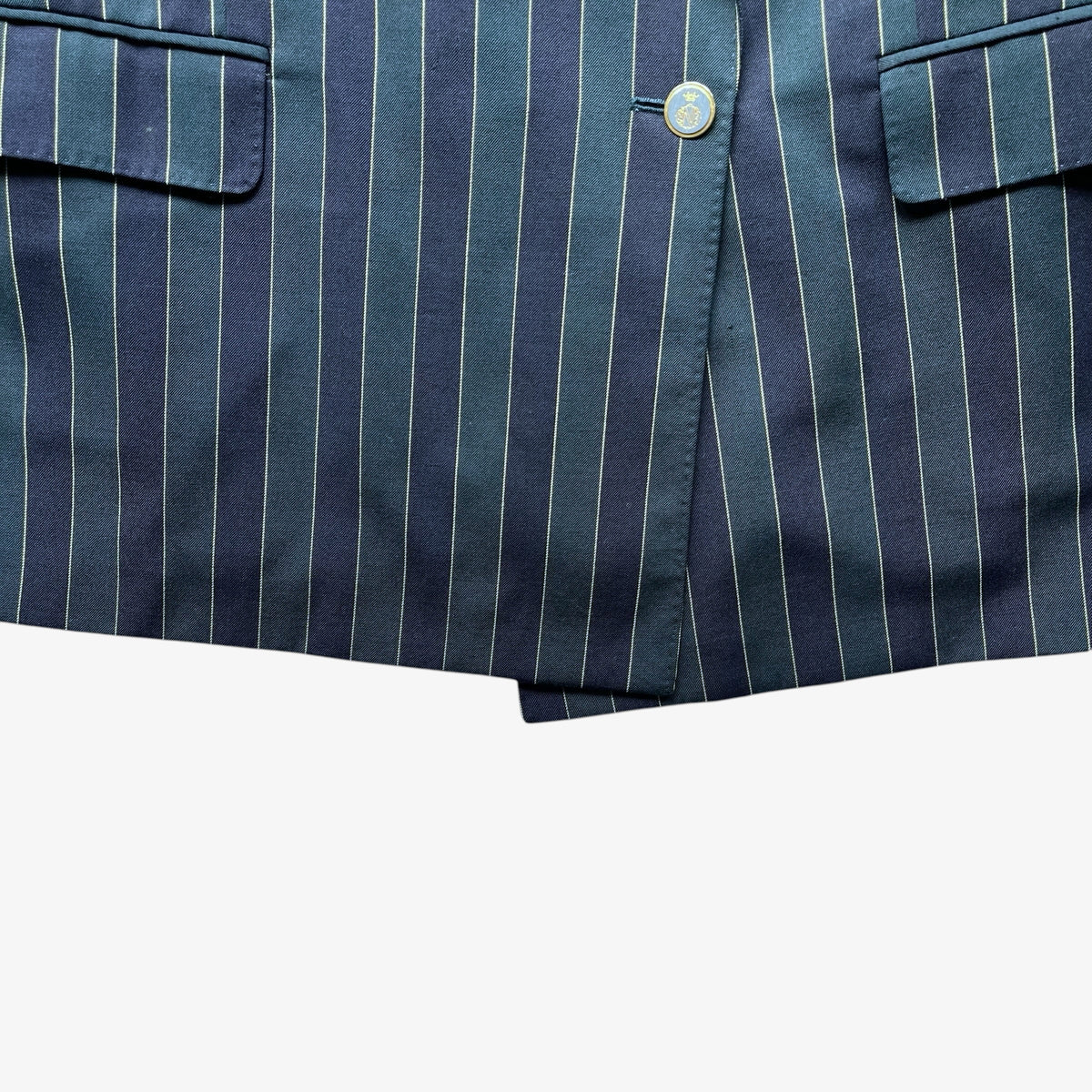 Close-up of a navy and green striped wool blazer, showing vertical stripes, a button closure, and part of a pocket on a plain white background.