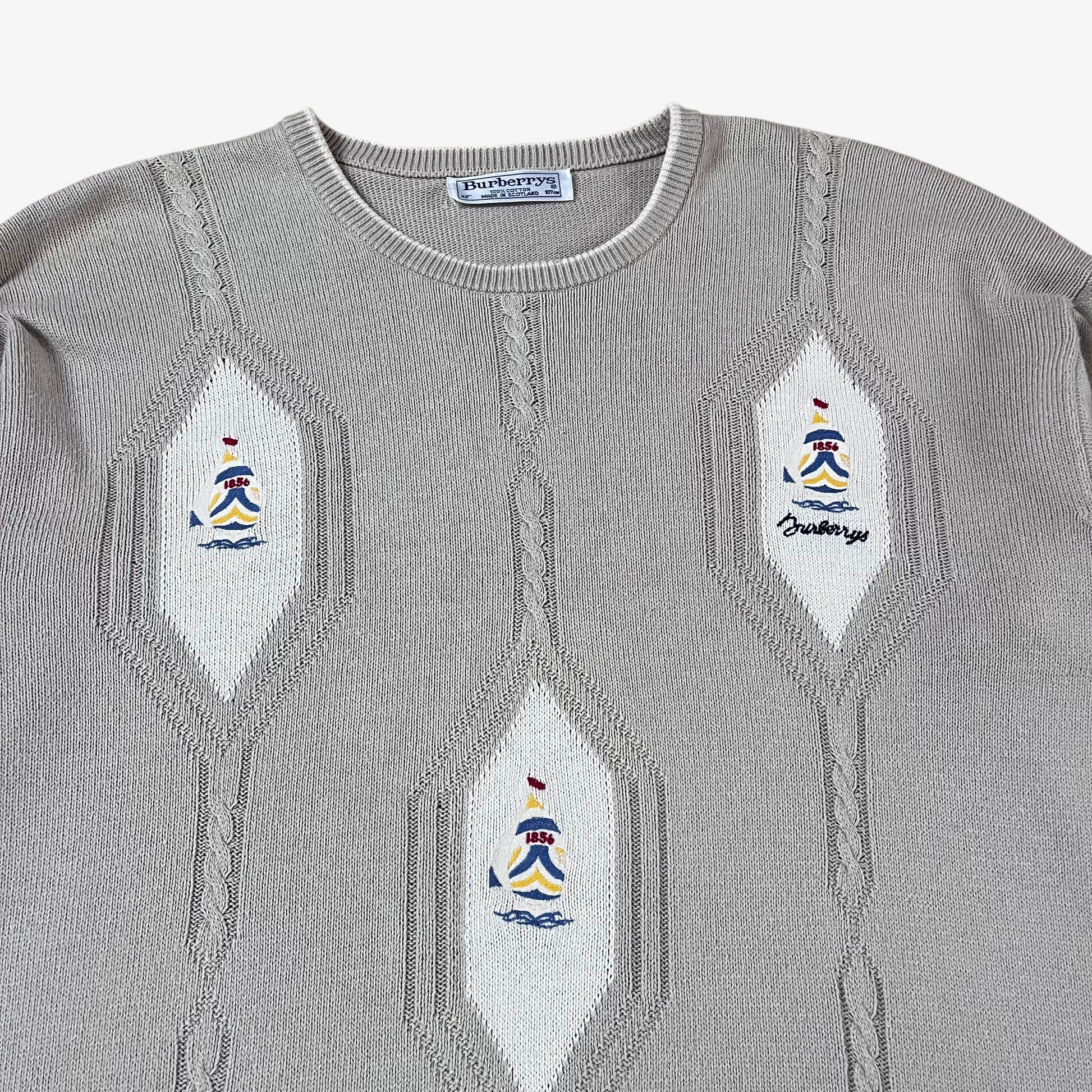 Close up of embroidered sailing motifs on vintage 80s Burberry men’s beige cable knit jumper.