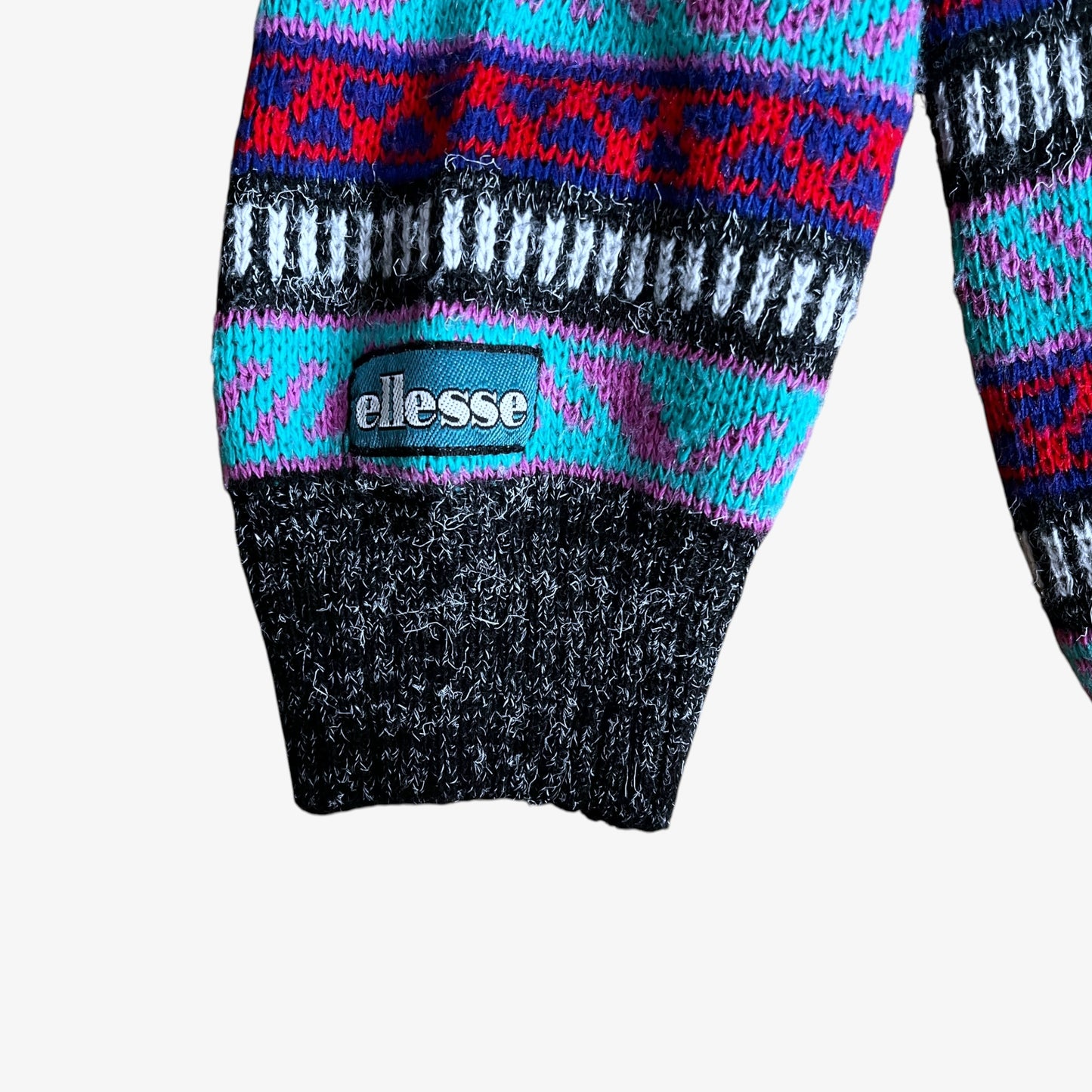 Close up of Ellesse logo embroidered on the cuff of a colourful patterned sweater.