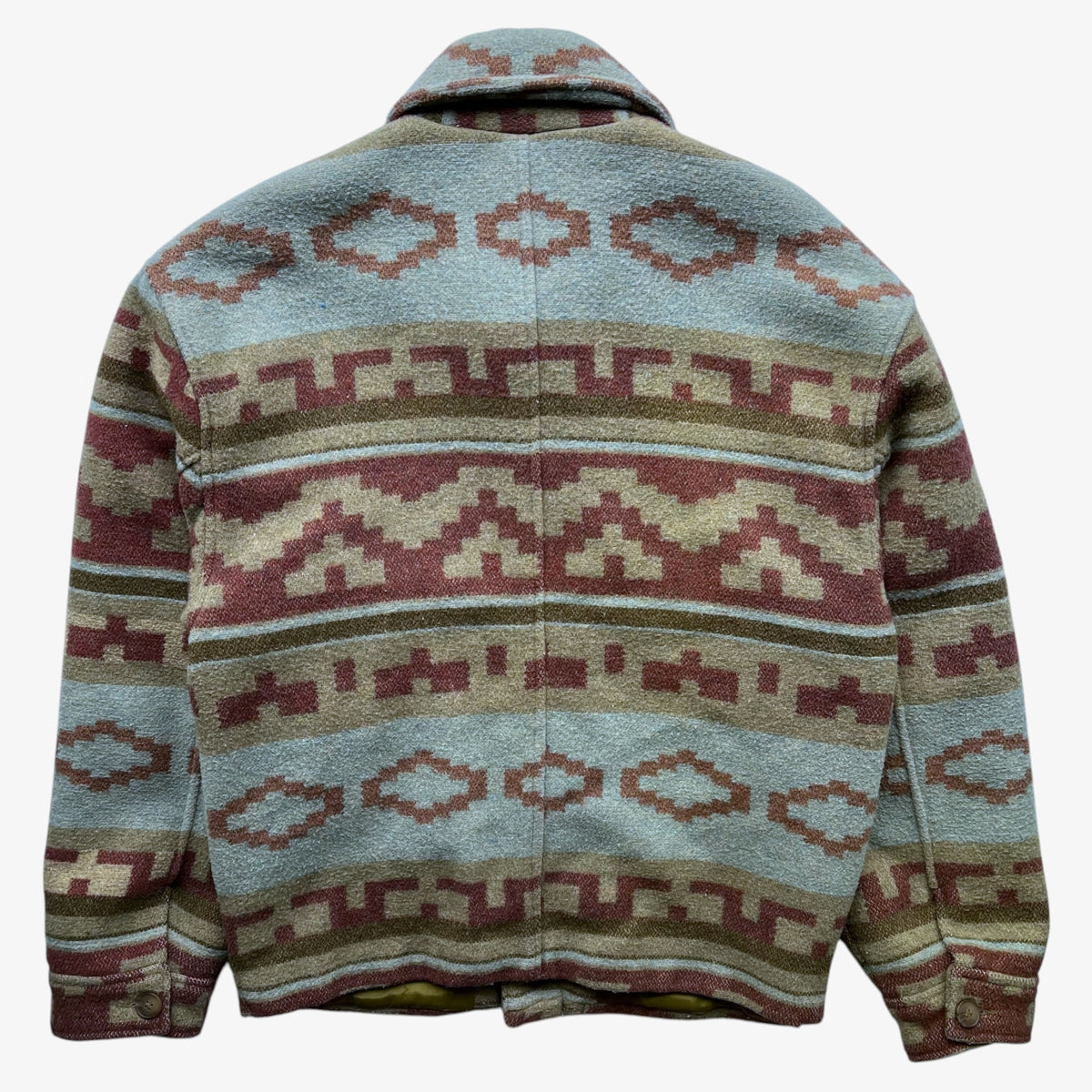 A wool jacket with a Southwestern navajo geometric pattern in muted shades of blue, terracotta, beige, and olive green, shown from the back against a plain white background.