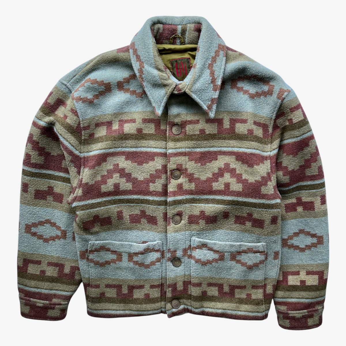 A button-front jacket with a collared neckline and two front patch pockets, featuring a Southwestern navajo geometric pattern in dusty blue, terracotta red, beige, and olive green on a white background.