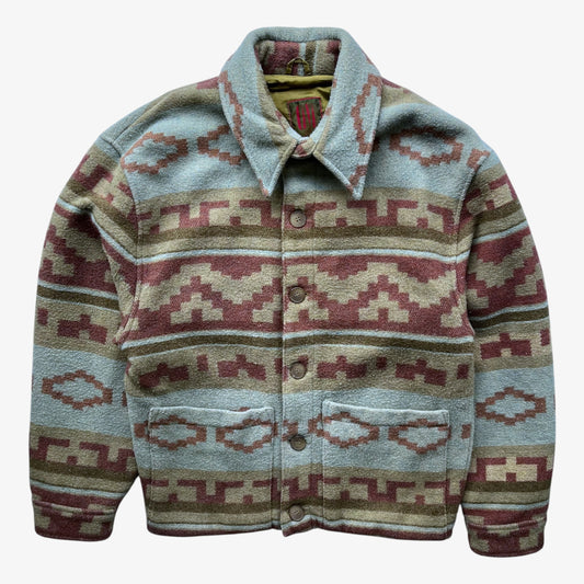A button-front jacket with a collared neckline and two front patch pockets, featuring a Southwestern navajo geometric pattern in dusty blue, terracotta red, beige, and olive green on a white background.