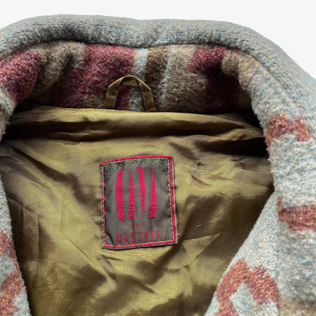Close-up of the interior of a wool jacket, showing a plush fuzzy trim in heather grey, dusty pink, and mauve, with an olive-brown inner lining and a sewn-on brand patch reading 'Oak Tree'.