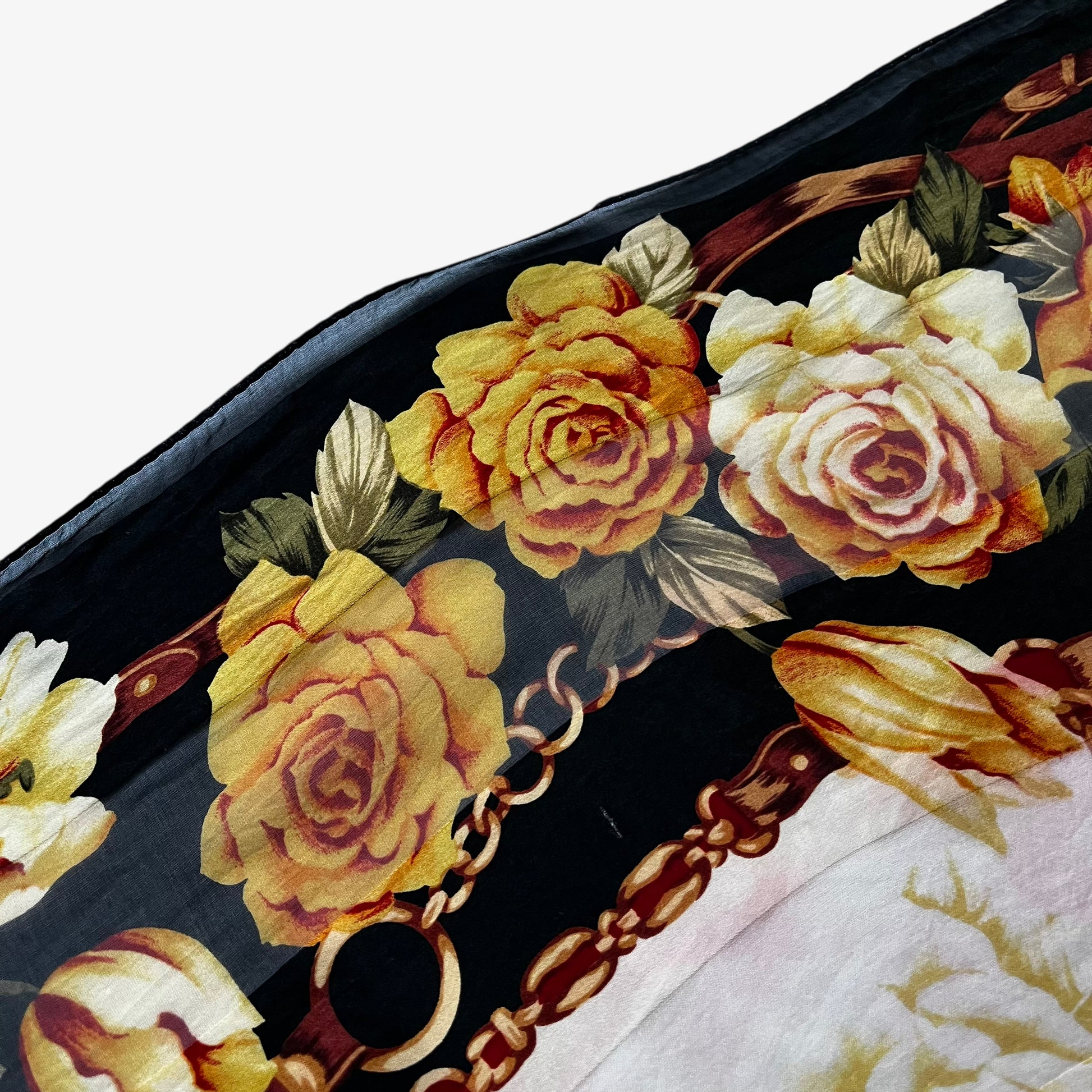 Patina on the hem of a women's vintage 80s Paolo Gucci black silk scarf featuring a checkered floral and equestrian buckle print.