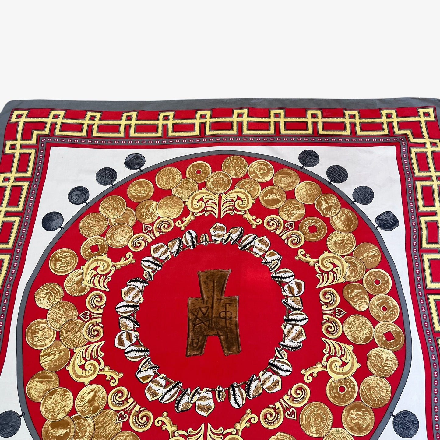 A square scarf featuring a bold red and gold coin pattern with a central bronze-like symbol, surrounded by gold coin motifs and bordered by white, grey, and black details.